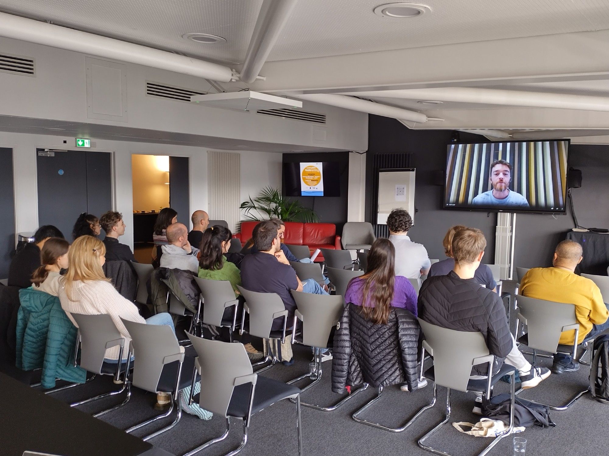 Seated crowd watching CuttingEEGs Max Chaumon start the conference on a screen.