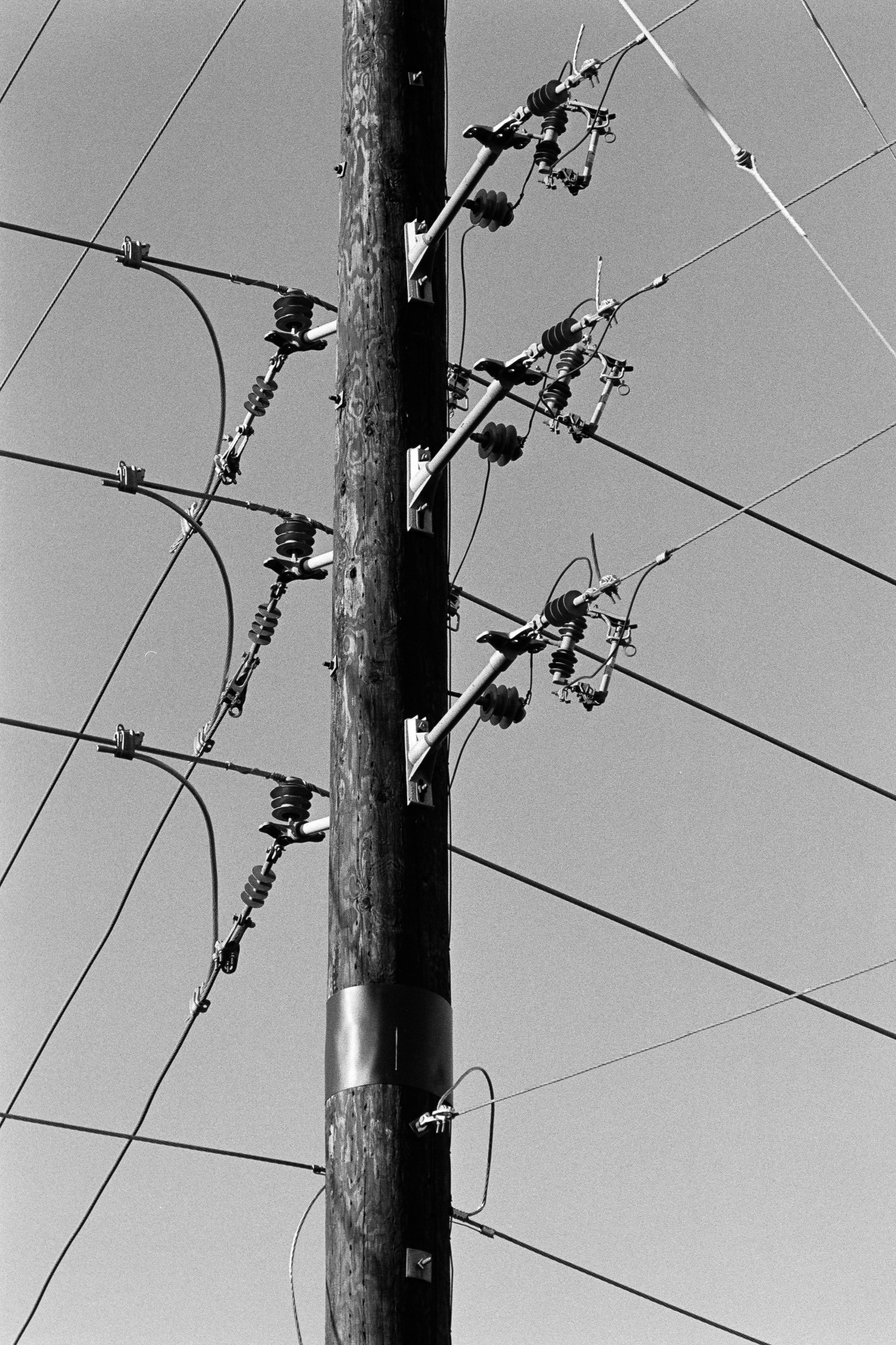 A black-and-white photo of a utility pole with many intersecting wires forming triangles and parallelograms against an empty sky