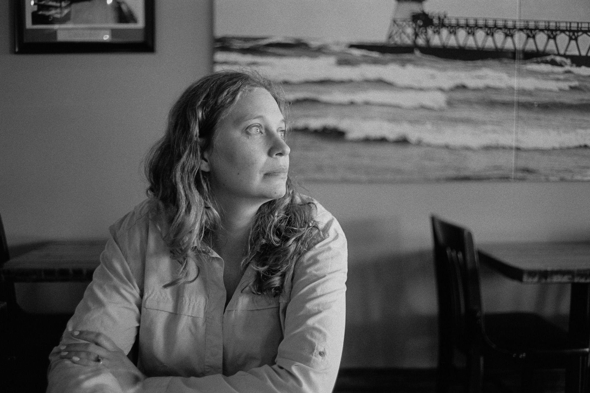 A black-and-white photo of a woman in a restaurant seating area looking over her shoulder towards bright light