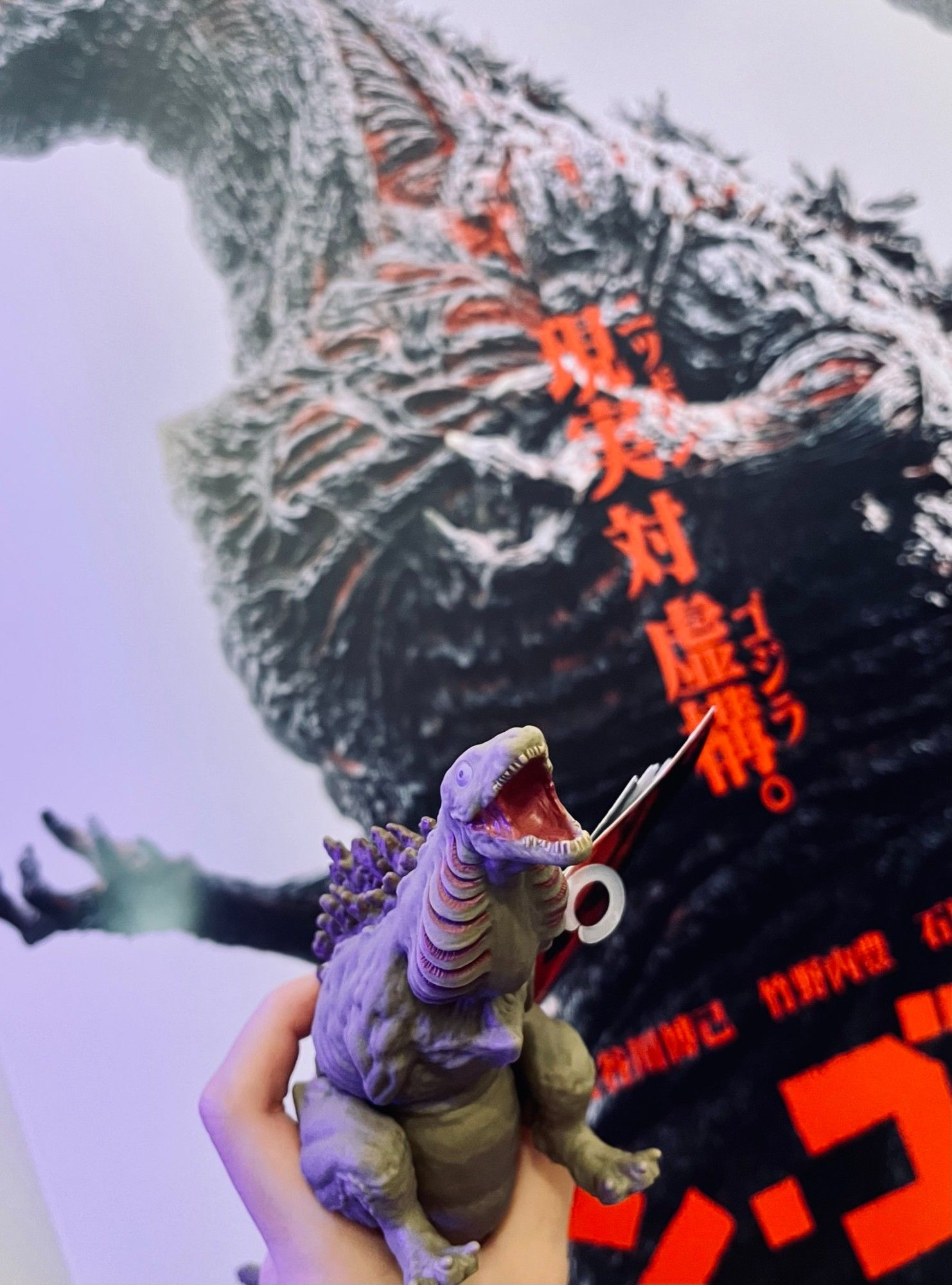 Photo of a Kamata-kun toy in front of a Shin Godzilla poster looking goofy as usual.