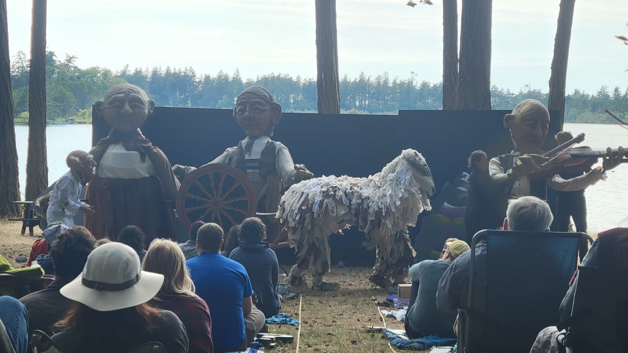 A scene from the climax with 3 giant puppets, the explorer, and a 2 person sheep costume. They sheared the sheep to make and spin celestial thread to help solve the conflict which was a tear in space caused by the CEO.