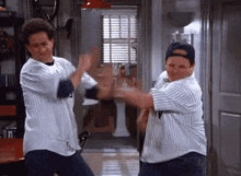 Jerry Seinfeld and George Constanza wearing baseball jerseys and slap fighting each other in his apartment