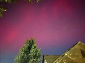 The Northern Lights glow pink over a rooftop. 