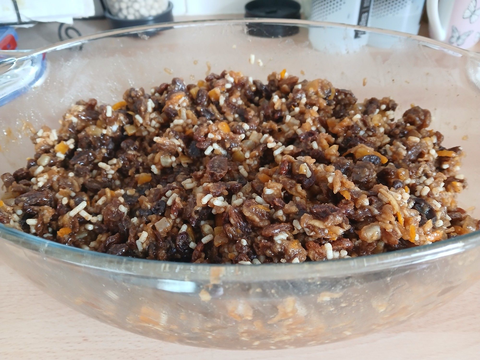 A large glass casserole dish full of mincemeat ingredients - raisins, sultanas, currants, dried peel, fresh orange and lemon zest, grated apples and vegetable suet (plus spices and brandy of course)