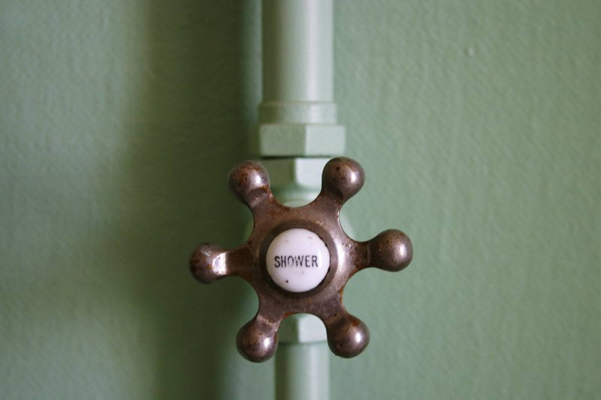 Colour photo of a green wall with a shower tap.