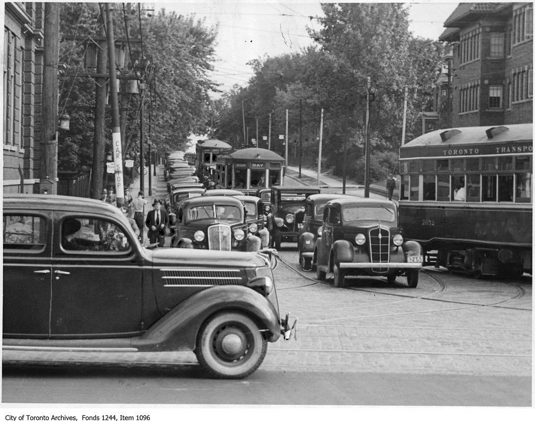 Black and white photo of 1930's cars in a traffic jam heading towards the camera. A few streetcars are also visible.