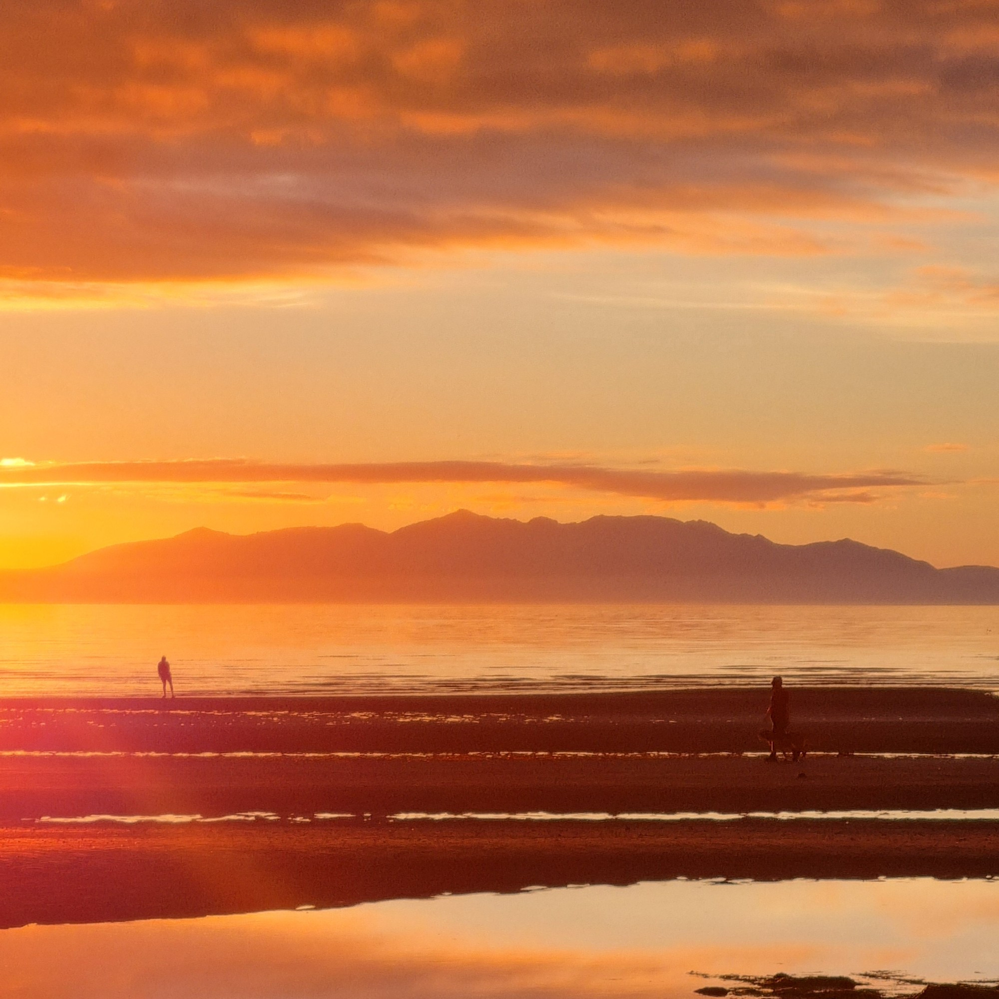 Sunset over the Isle of Arran from Barassie, South Ayrshire, with two figures on the beach in the middle distance taking in the view