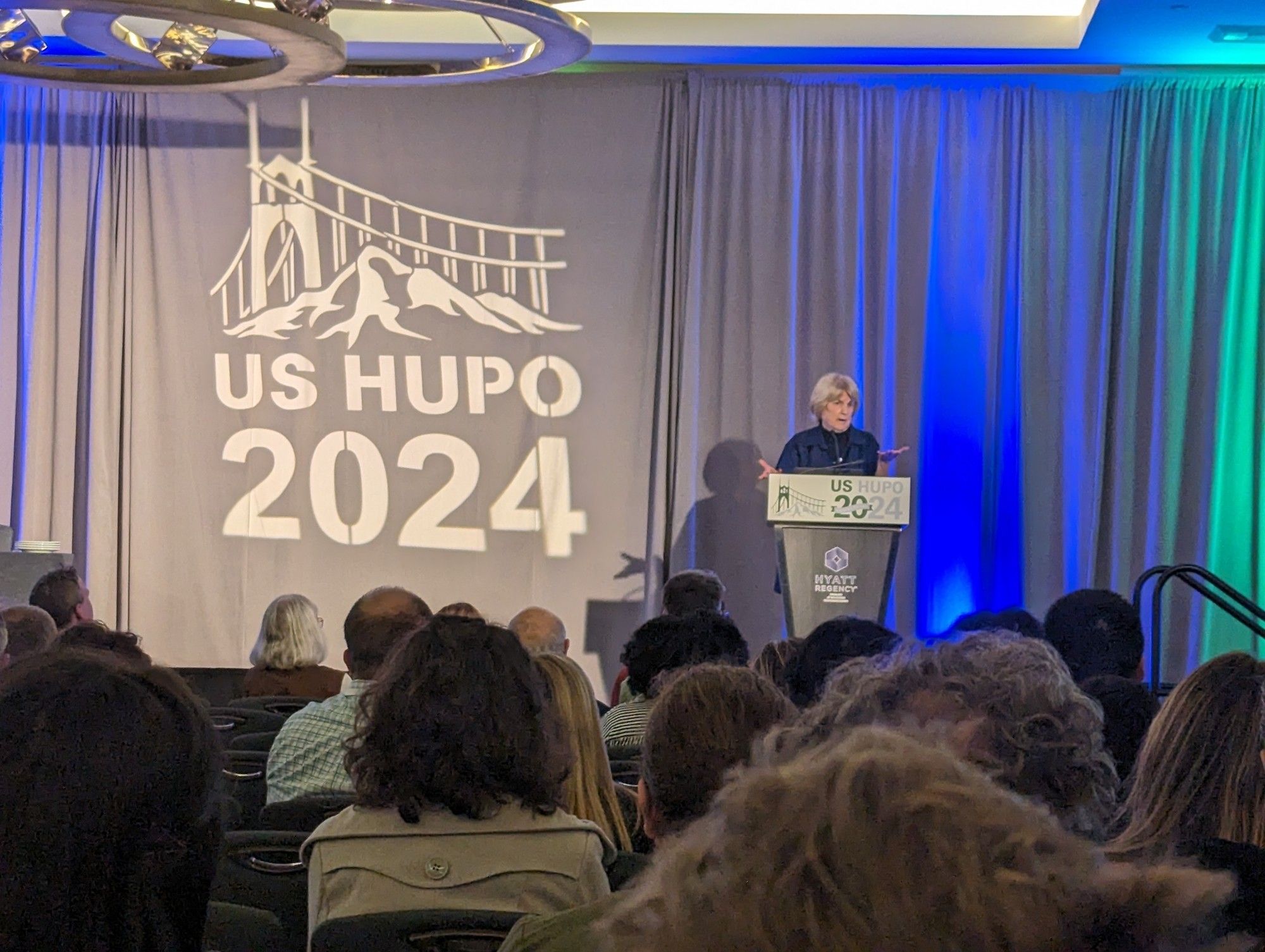 Mary Claire King at a podium giving the keynote for US HUPO 2024