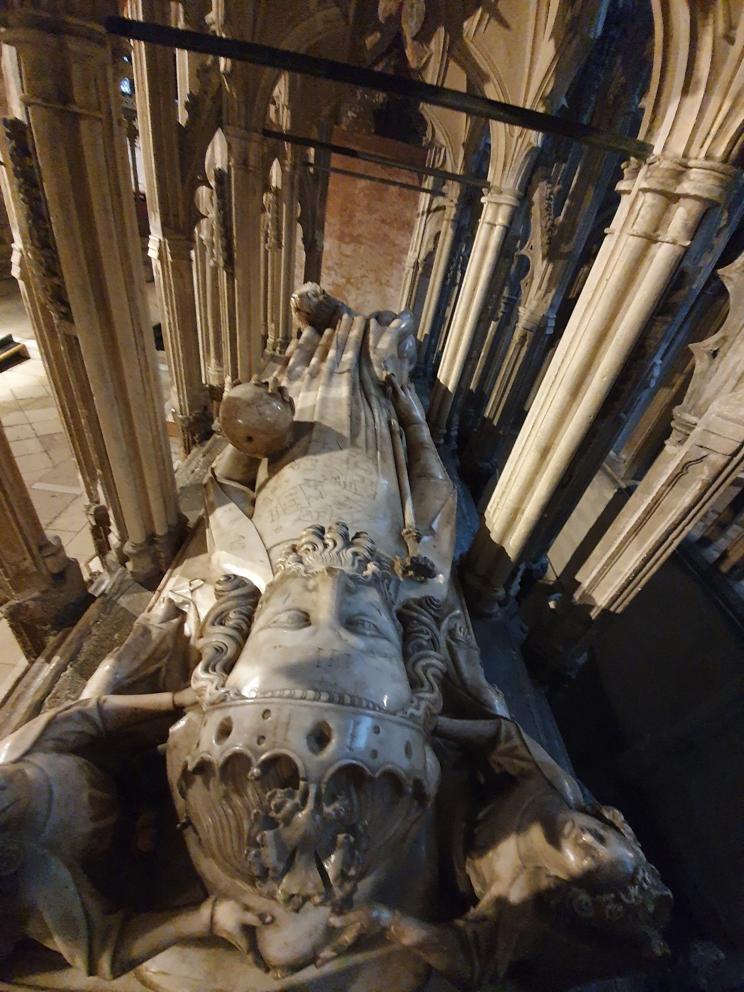 The alabaster effigy of King Edward II on top of his tomb, with his crowned head in the foreground and his body tapering away into the distance under a series of arched columns. Lots of graffiti can be seen scratched into the alabaster body.