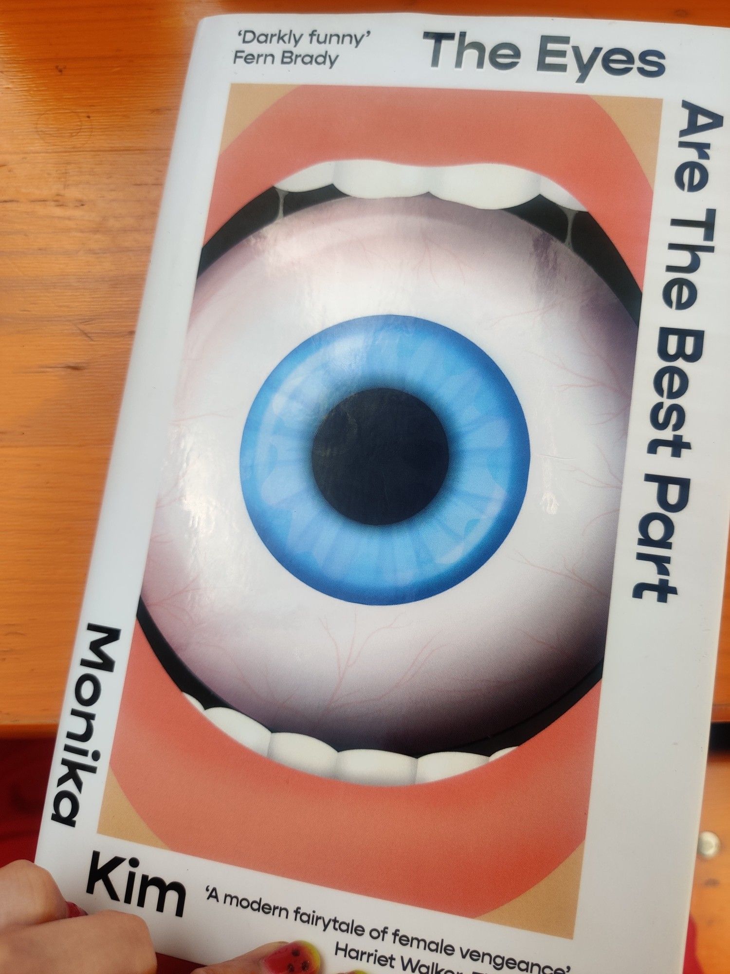 A picture of the book THE EYES ARE THE BEST PART by Monika Kim. It's a hard back book with an open mouth holding an eyeball