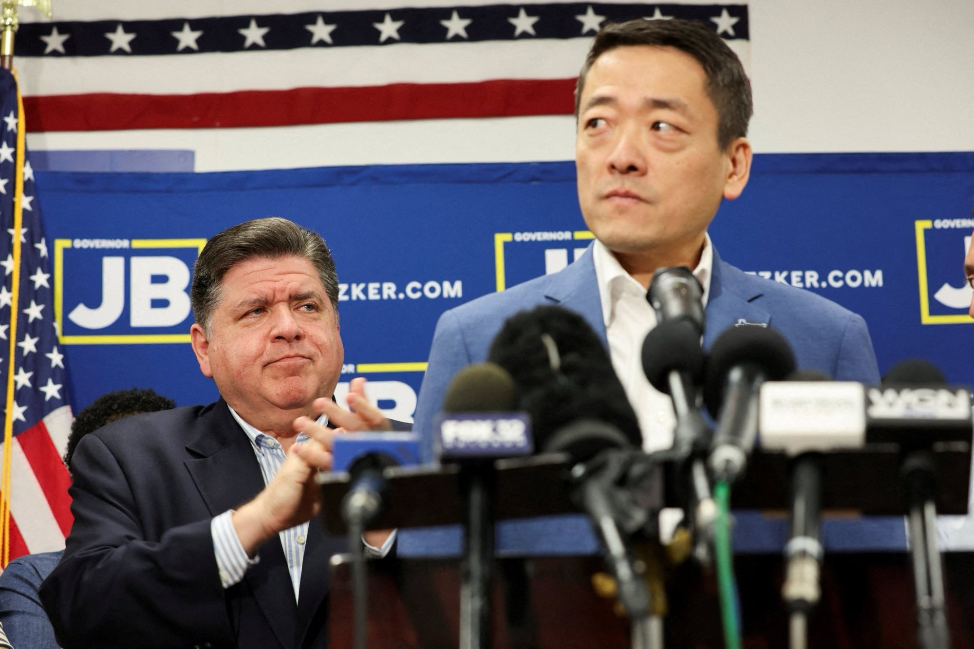 Image of Gene Wu standing at a podium as J.B. Pritzker looks on.
