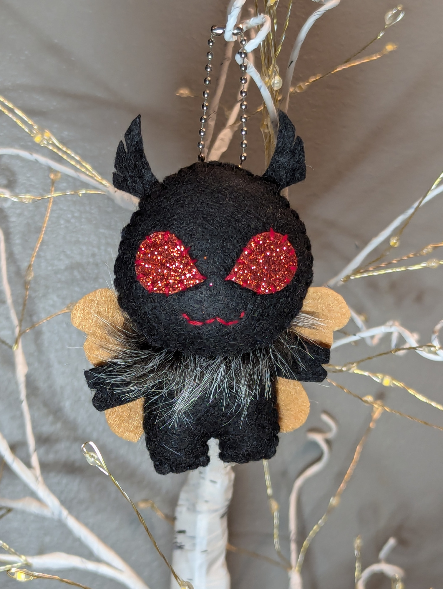 Mothman is made from black felt. He has brown felt wings and big red sparkly eyes. He also has a grizzled black and white ruff. His antennae are black and very cute. 