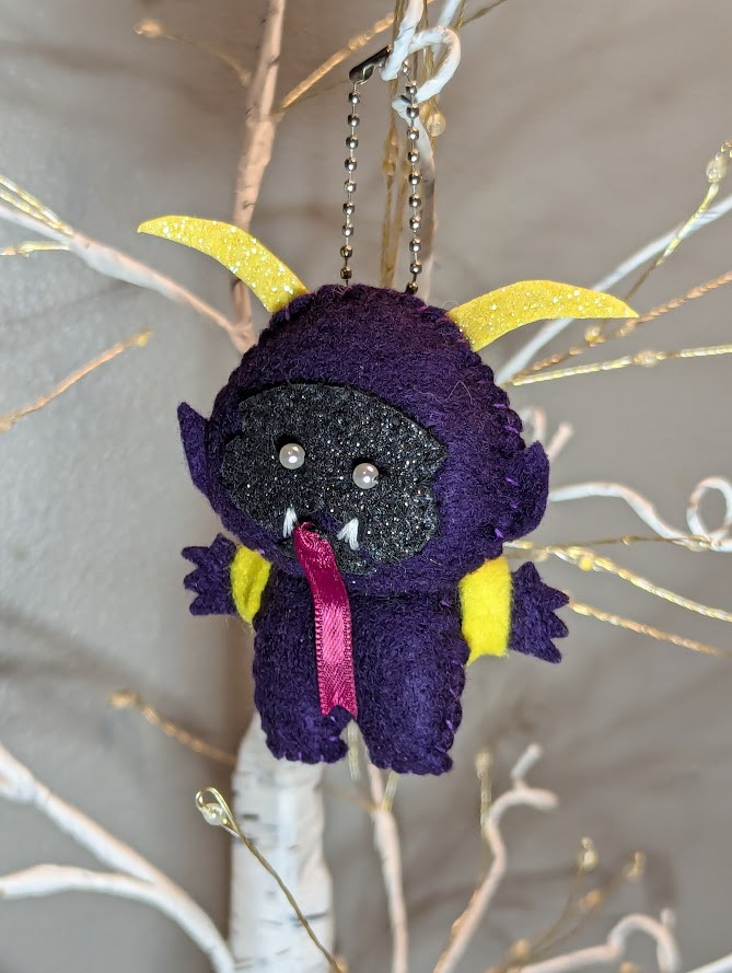 It's Krampus! He's midnight purple felt with a charcoal/black sparkly face. He has yellow horns that match his little backpack for carrying away tiny naughty children. (Tiny naughty children are included)