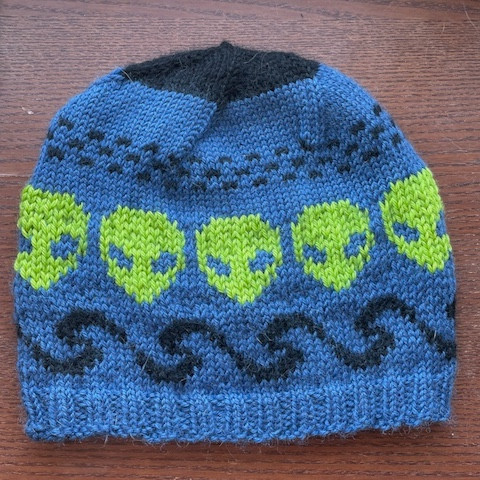 A light blue beanie with a pattern of darker blue waves and acid green alien heads. 