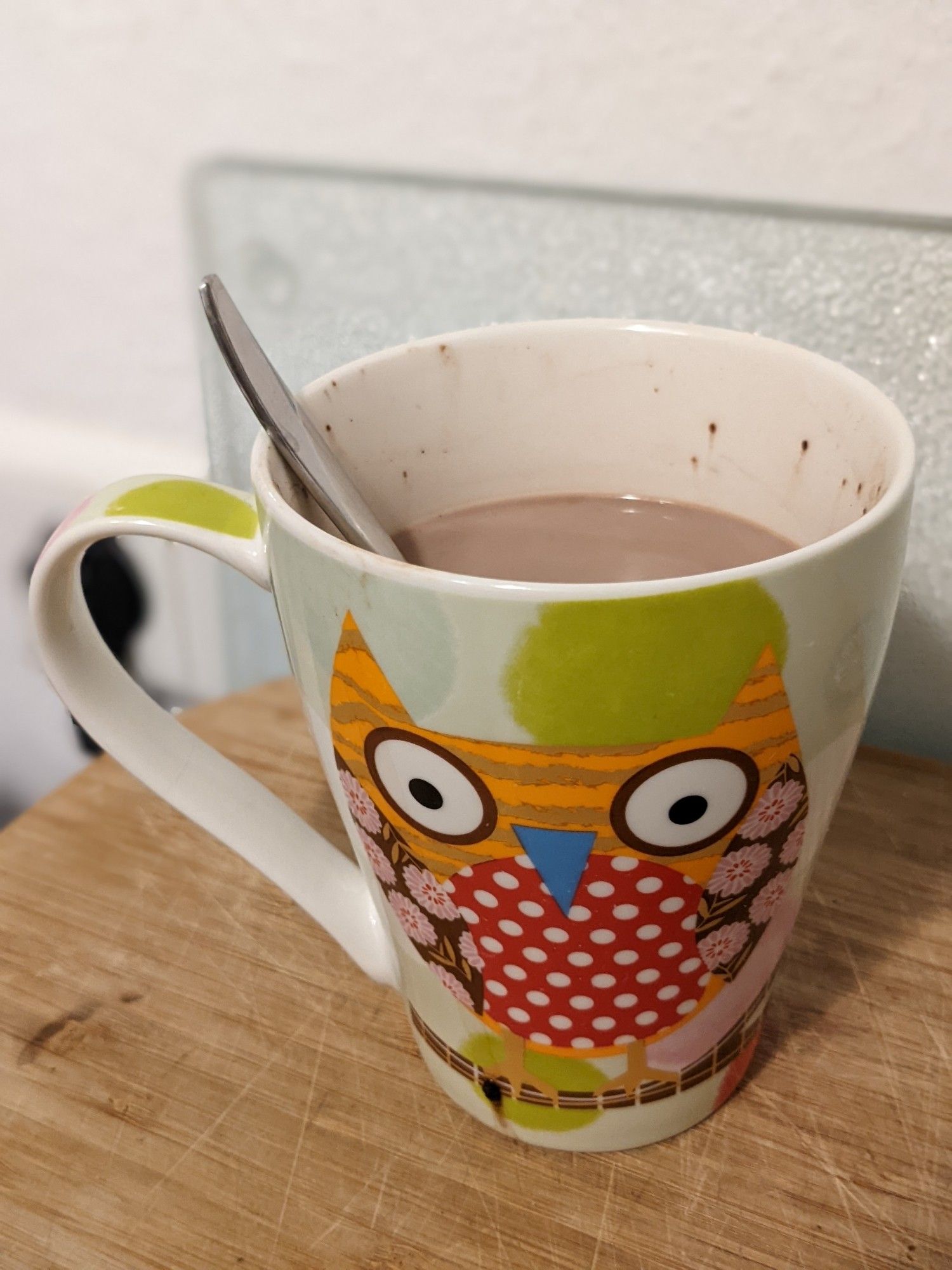 Tasse mit grüner Eule und Kaba drin auf Holz