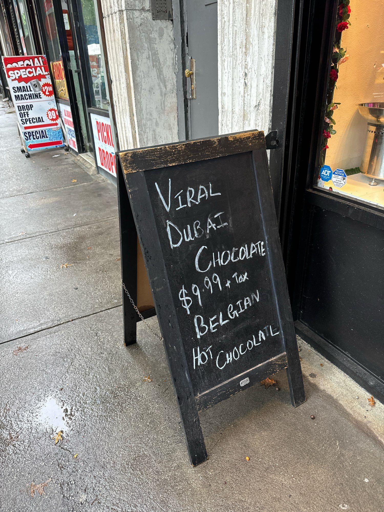 A chalkboard outside a store that says 

VIRAL DUBAI CHOCOLATE $9.99 + tax
BELGIAN HOT CHOCOLATE