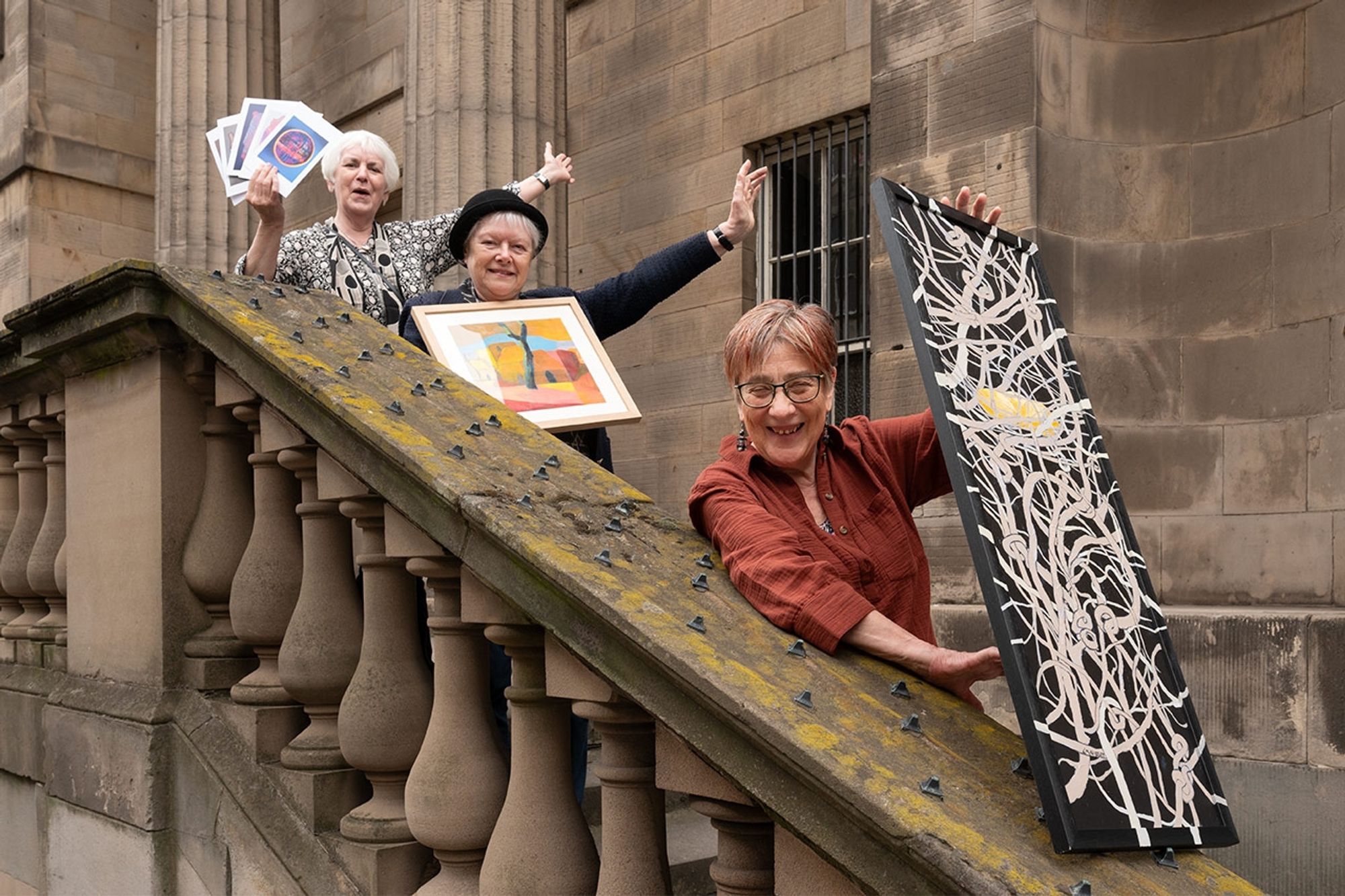 An Open House event at Leith Custom House. Three people are standing on the steps outside the building, holding their artwork up. Credit - Scottish Historic Buildings Trust.