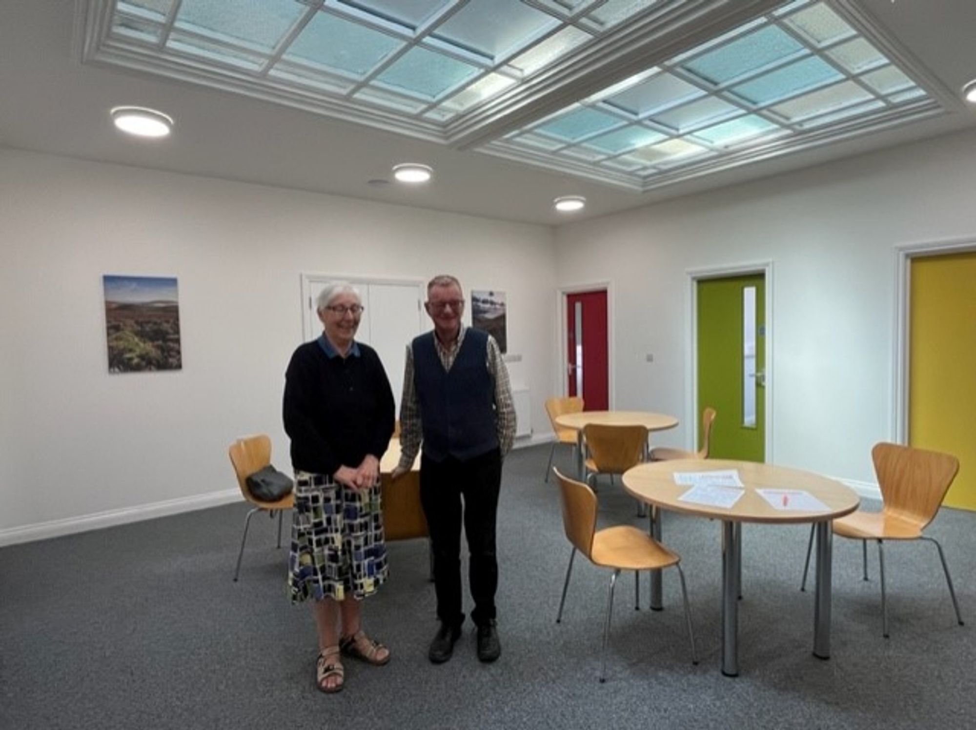 The Enterprise Hub Offices after the Energise Project renovations. Two people are stood smiling in front of three desks in a well-lit, restored space.