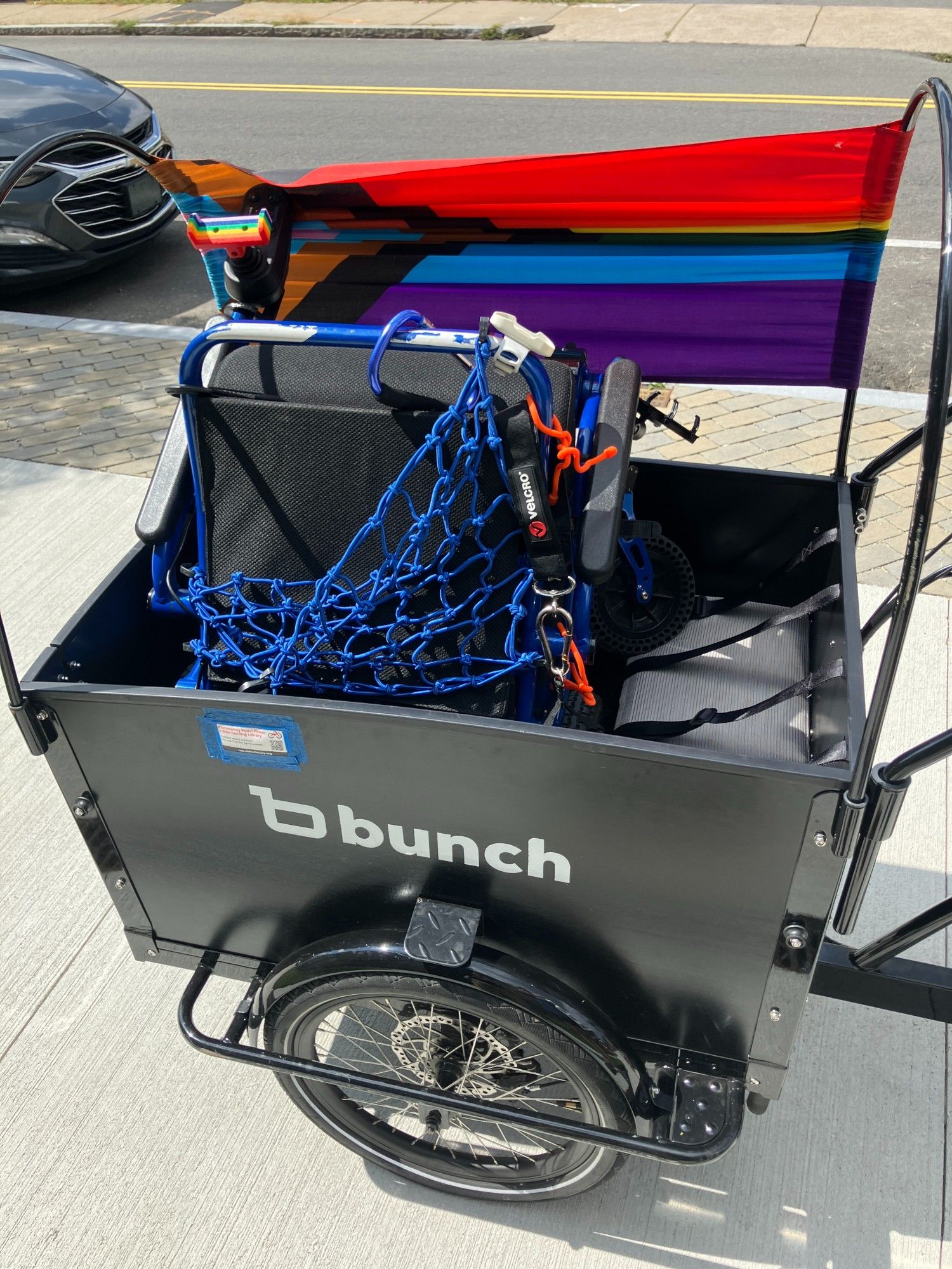 A side view of the front bucket of a cargo trike, with a wheelchair folded up in the bucket.