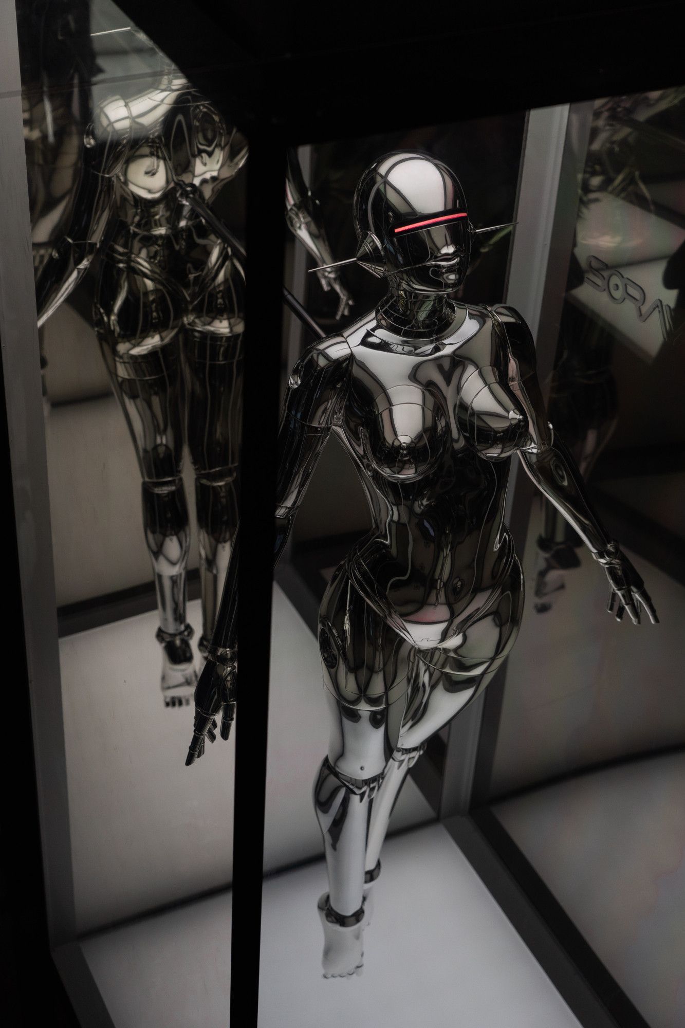 Black female robot made of shiny black metal with a red light instead of eyes in a floating like postion in a long box made of mirrors and glass. View from left angle above.
Photo by Xu Haiwei on Unsplash