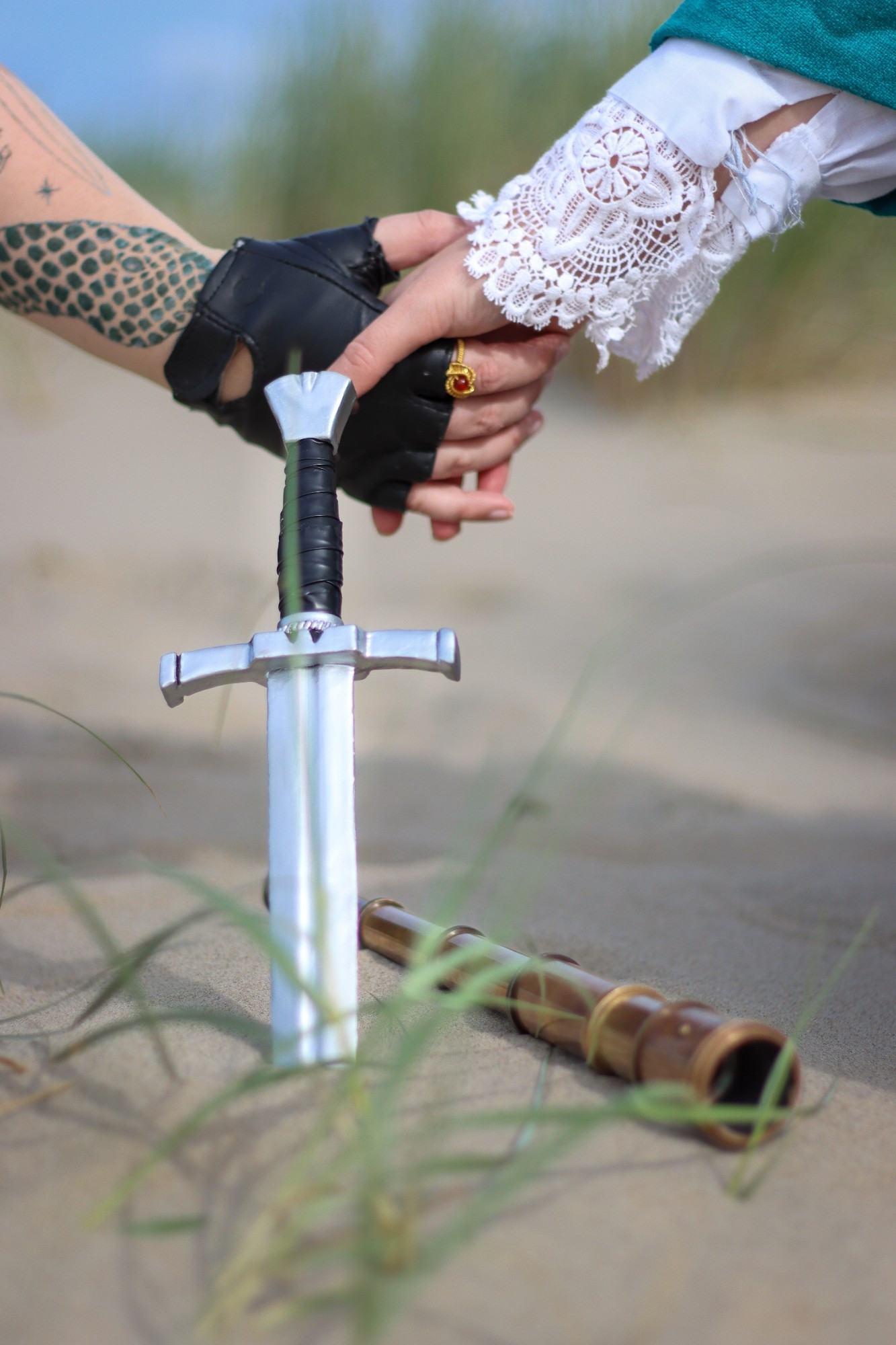 Blackbeard cosplayer and Stede cosplayer holding hands with Blackbeard's knife and Stede's spyglass on the sand in front