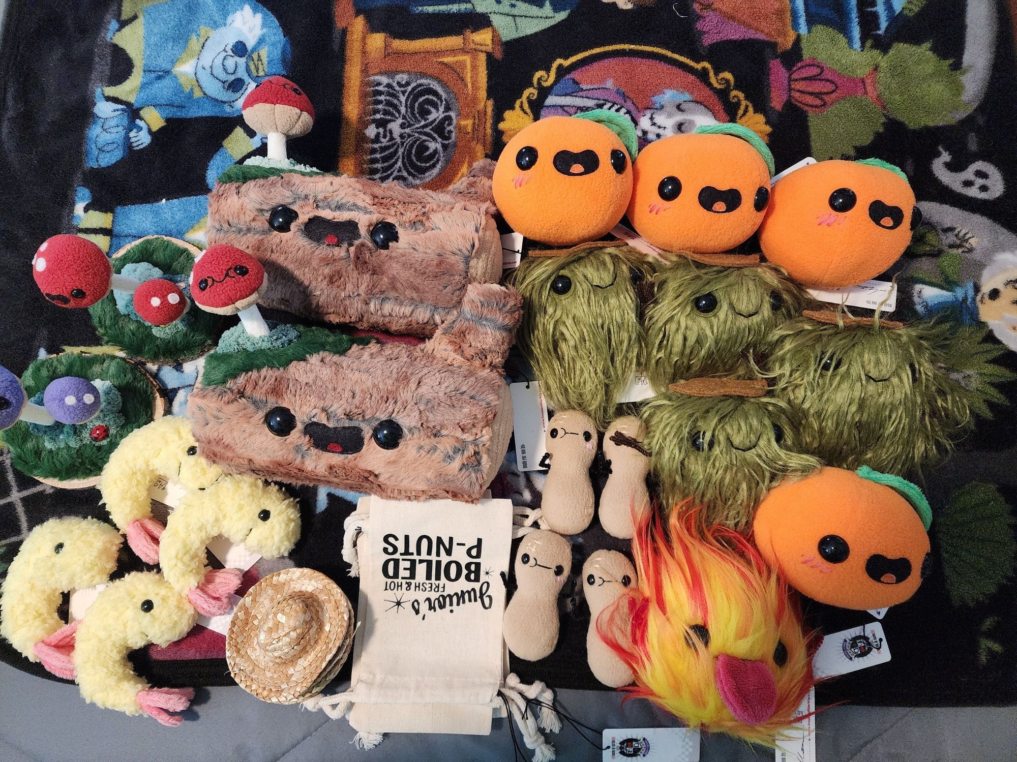 Large group of handmade plush laid out on a bed, all smiling: two big fuzzy mushroom topped logs, two mushrooms on moss bases, 4 fluffy fried shrimp, peanuts with bags, a fireball, 4 oranges, and 4 moss creatures