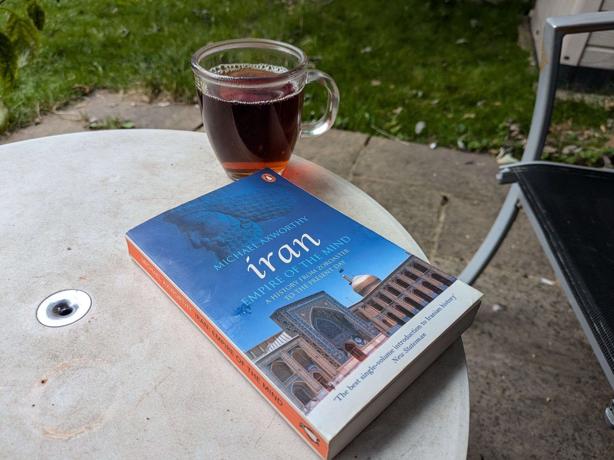 A small paperback book showing a mosque under bright blue skies and a glass of dark milkless tea