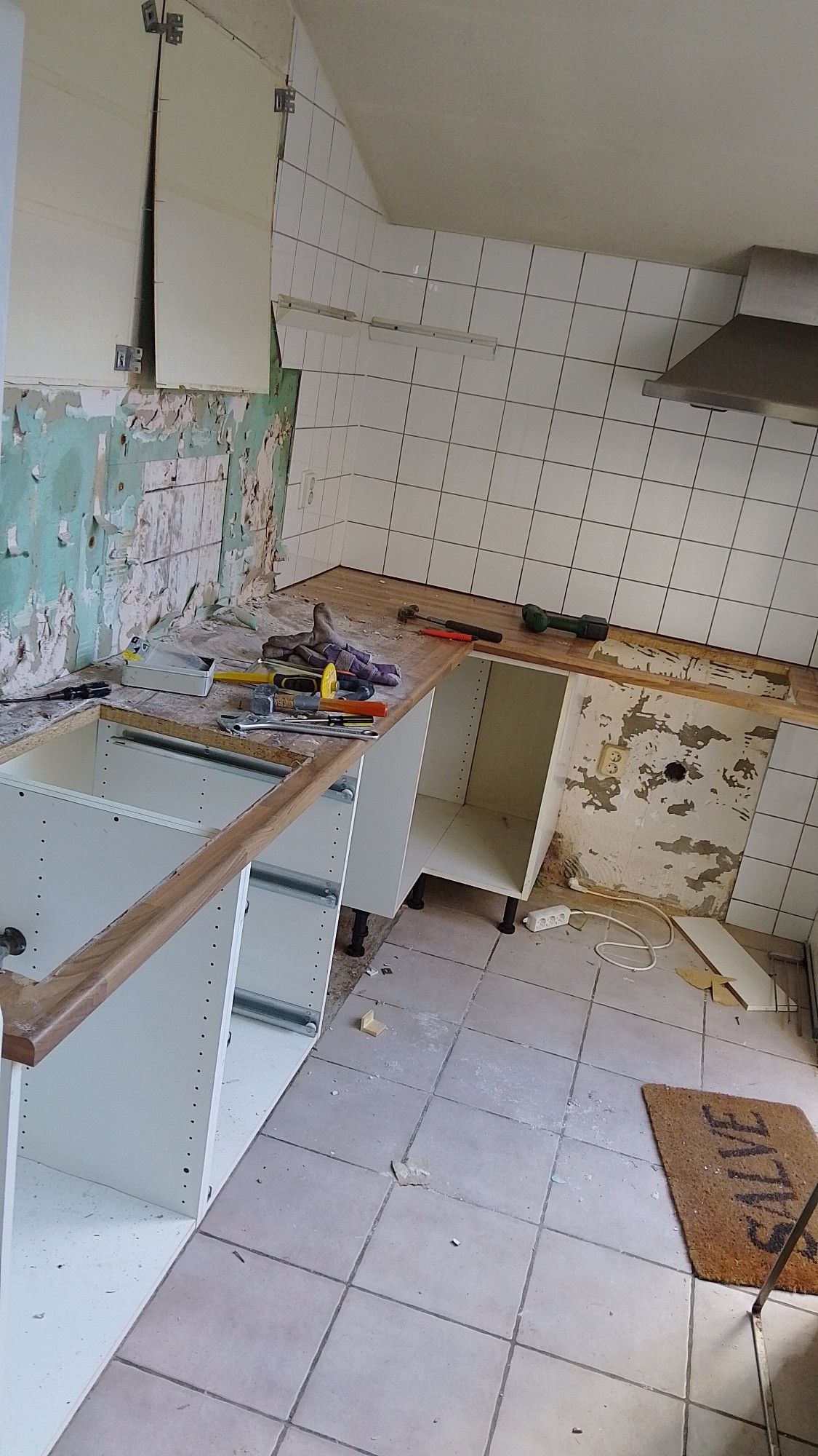 Een foto van een keuken die afgebroken wordt. De keukendeurtjes zijn weg, met als de oven en de wasbak. Op het aanrecht liggen verschillende soorten gereedschap