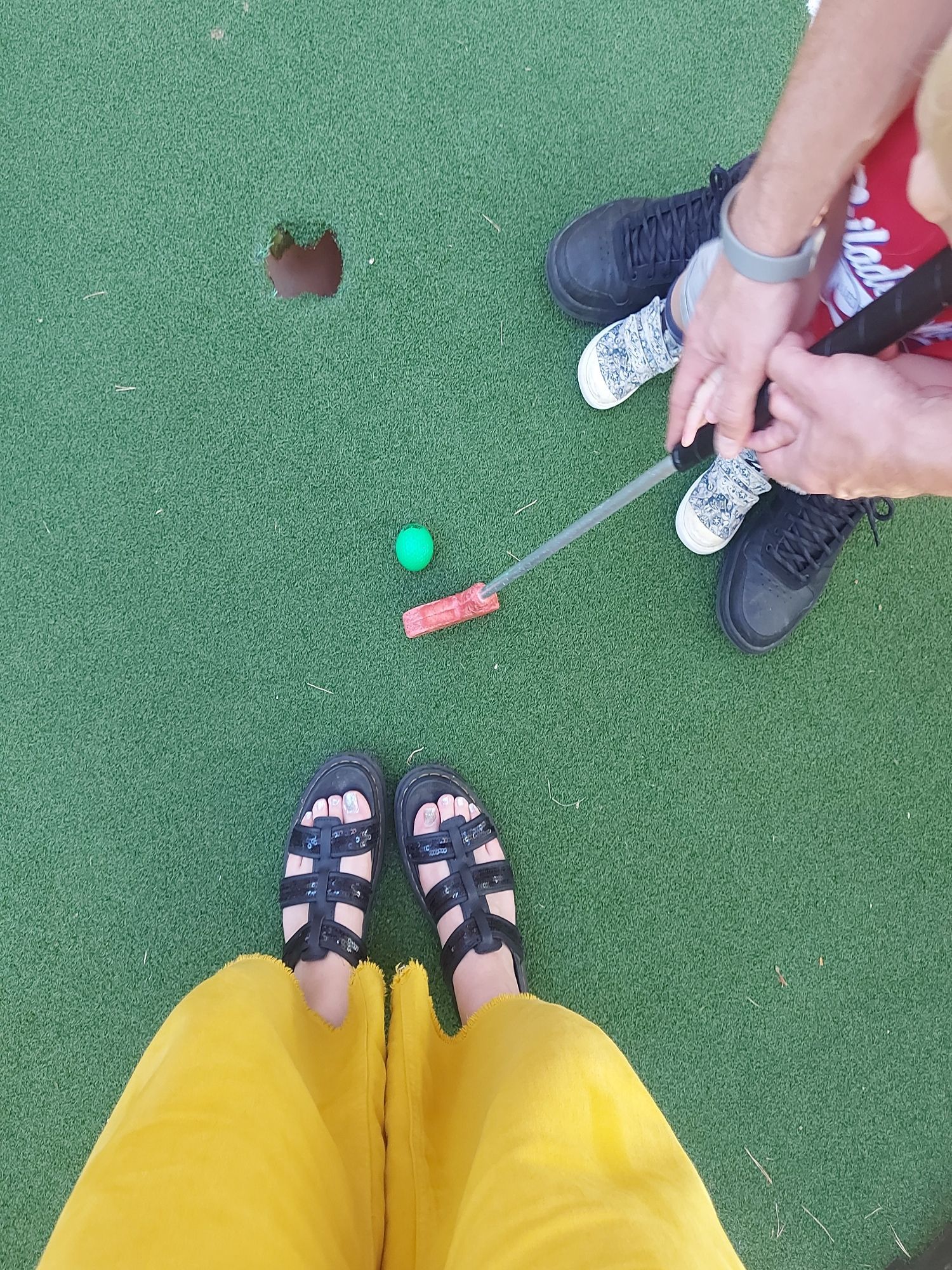 Photo of feet and putting a golf ball into a hole