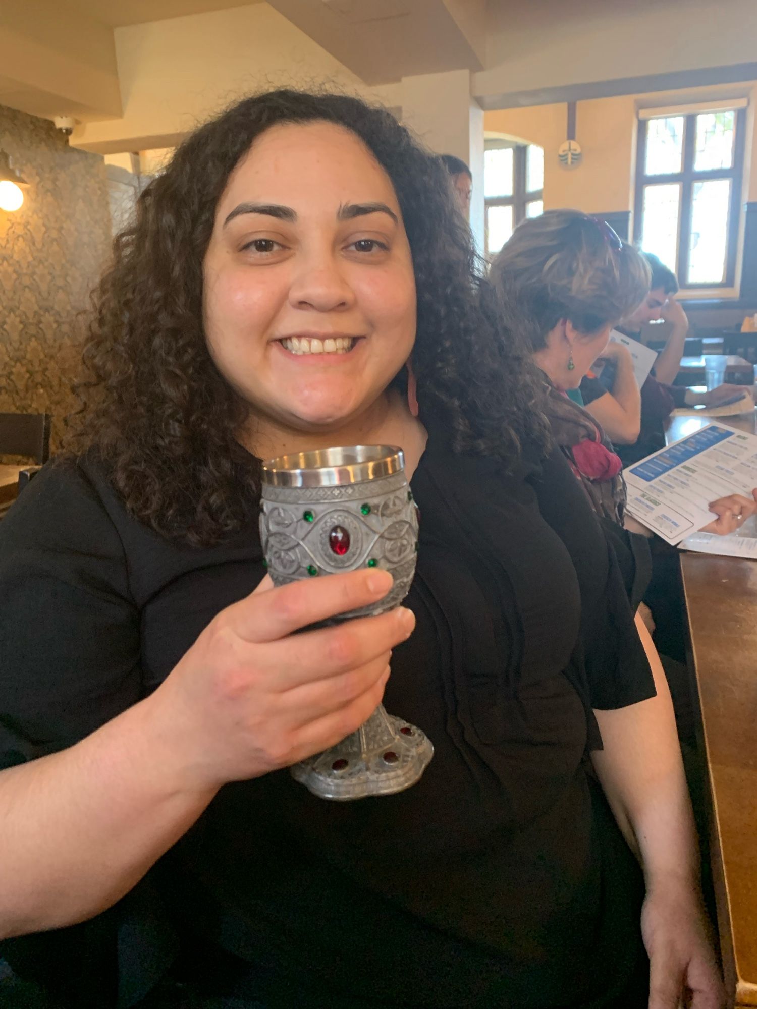 Dr Andrea Murillo Ramos after her successful defence. She is in the graduate pub, holding a chalice, full of smiles and toasting her success