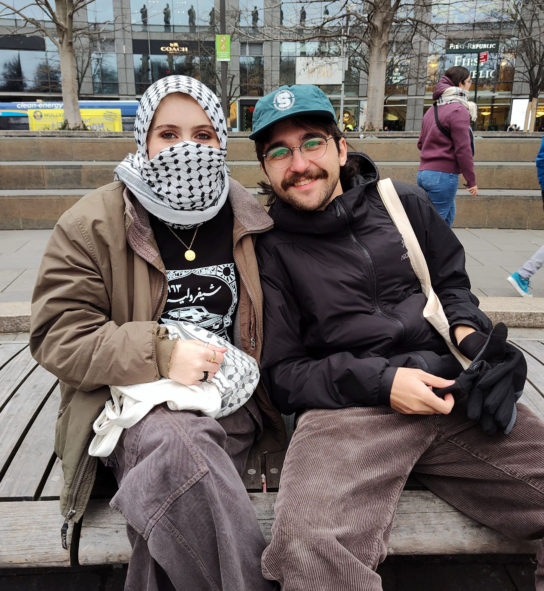 Two activists pose for a photo one activist has a keffiyeh wrapped around their head and most of their face except for the eyes and the person with them has a camera