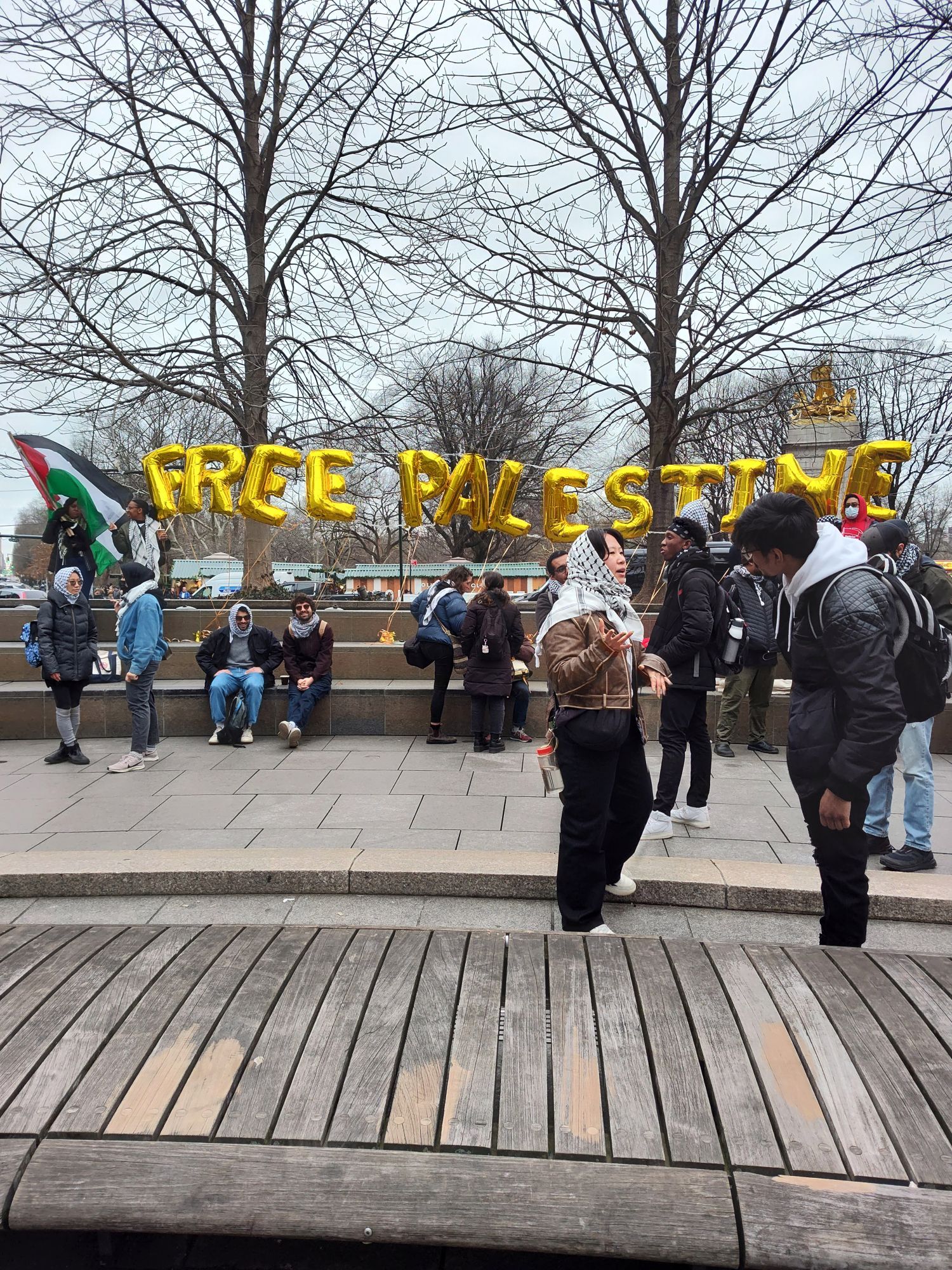 photo is taken outside in Columbus Circle in New York City. I'm trying to keep my distance because of COVID, but you can see people are starting to gather at the protest and there's a golden metallic balloon that reads Free Palestine where it's spelled out puffy letter by letter