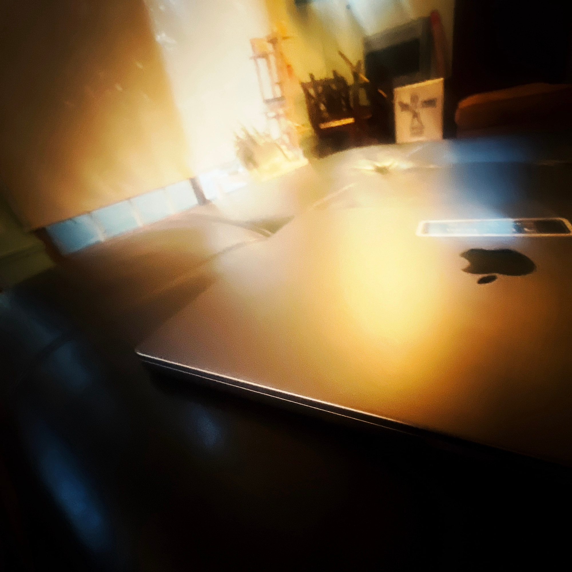 A shiny black Apple laptop with a yellow light reflecting off it. 