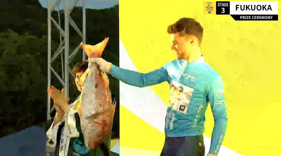 Cyclist on podium holds up sea bream fish prize.