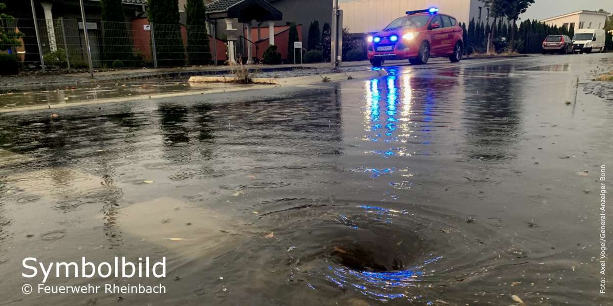 Symbolbild. Wasser steht auf einer Straße. Im Hintergrund ein Feuerwehrfahrzeug.