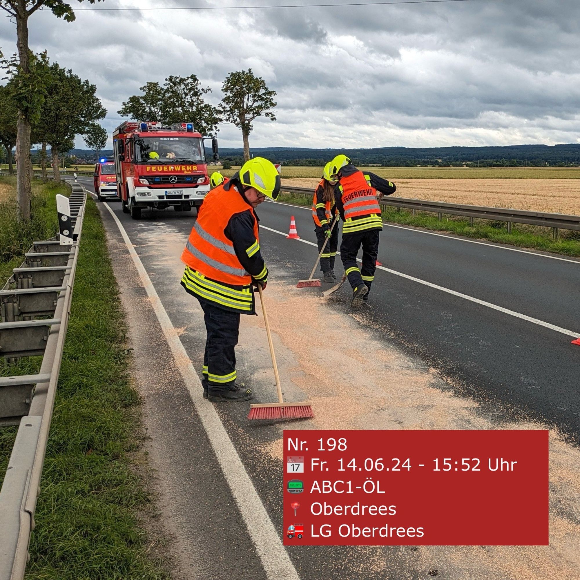 Feuerwehrleute fegen mit Besen Ölbindemittel auf einer Straße zusammen. Im Hintergrund ein Feuerwehrauto.