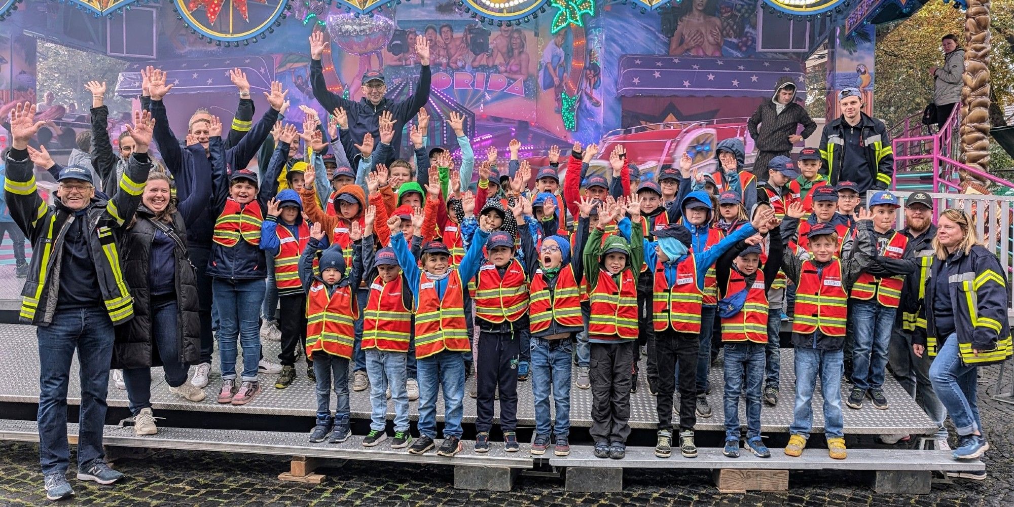 Gruppenfoto der Kinderfeuerwehrmitglieder mit den Betreuer:innen vor einem Karussell.