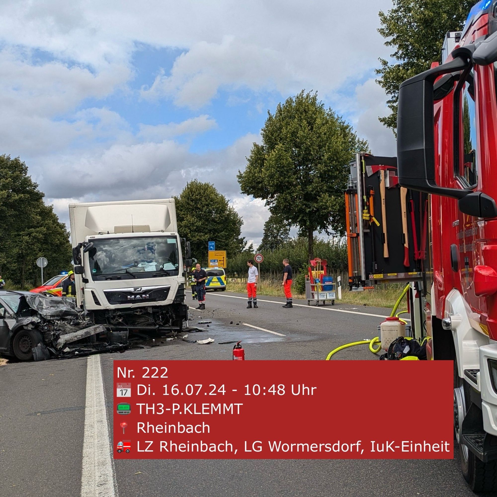 Foto eines Verkehrsunfalls. Im Vordergrund recht ein Feuerwehrauto. Hinten links ein verunfallter PKW sowie ein LKW.