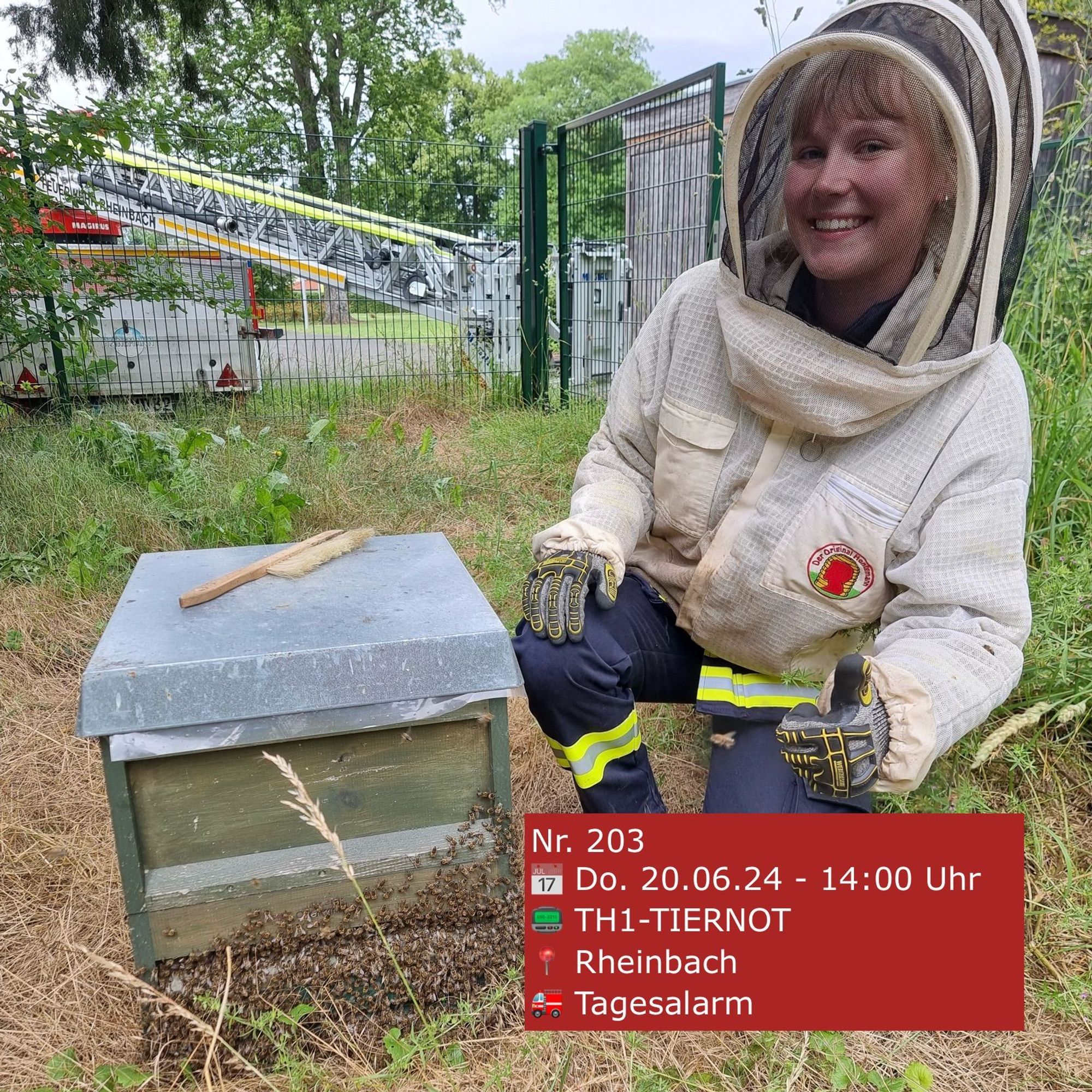 Eine Feuerwehrfrau mit einem Imkeranzug neben einem Bienenstock.