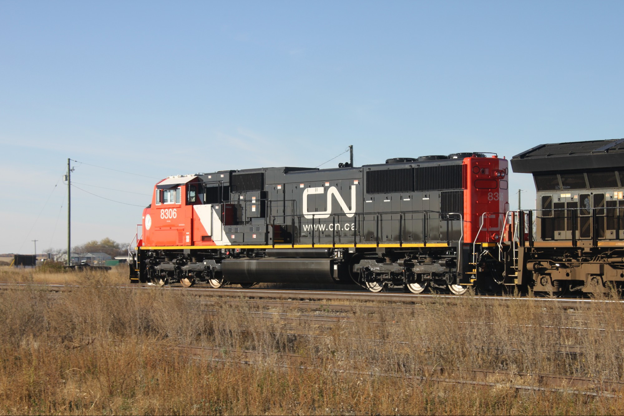 A freshly rebuilt CN 8306 leads A405 west out of Rivers, MB. Seen in front of some grain bins.