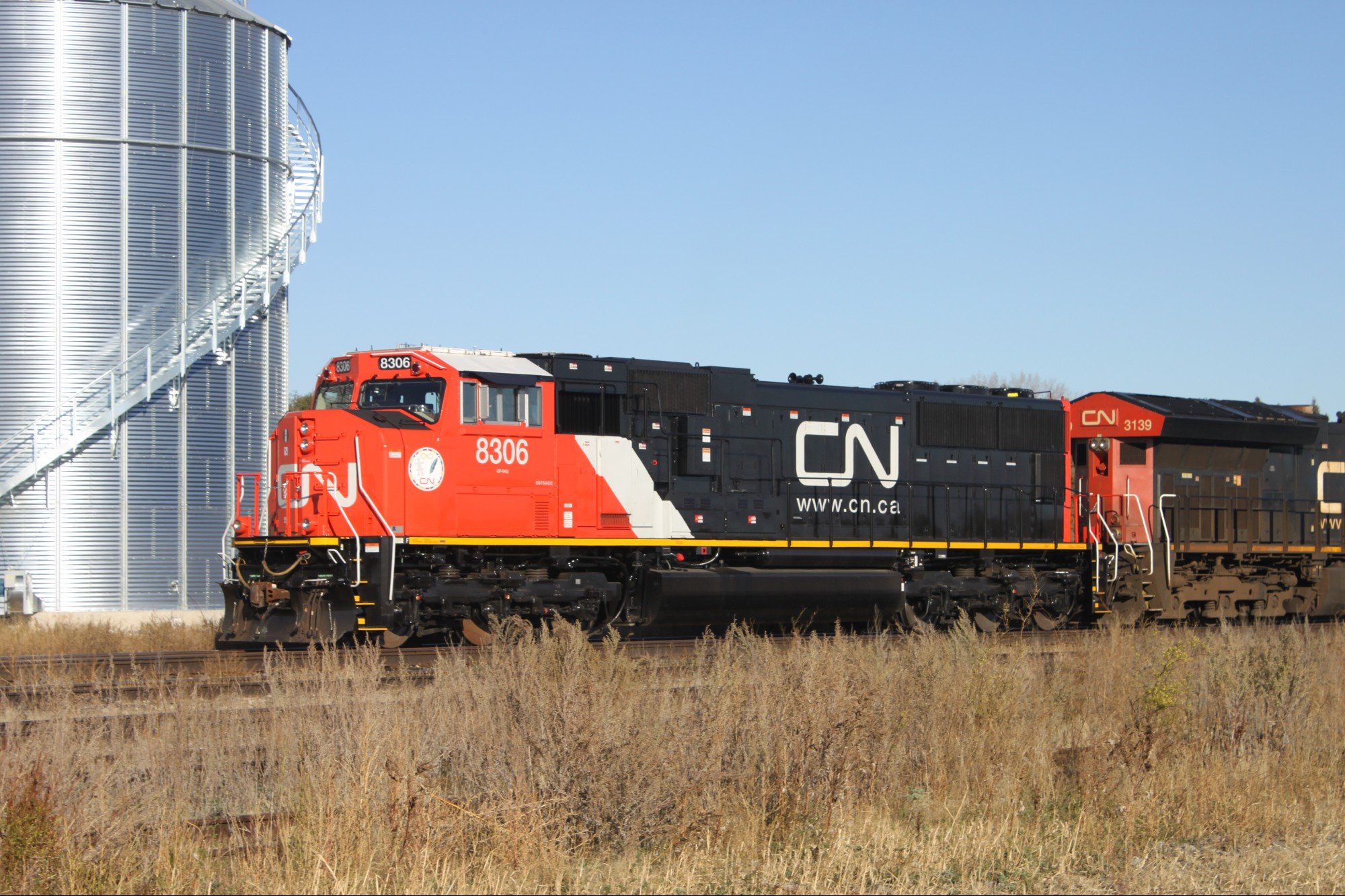 A freshly rebuilt CN 8306 leads A405 west out of Rivers, MB. Seen in front of some grain bins.