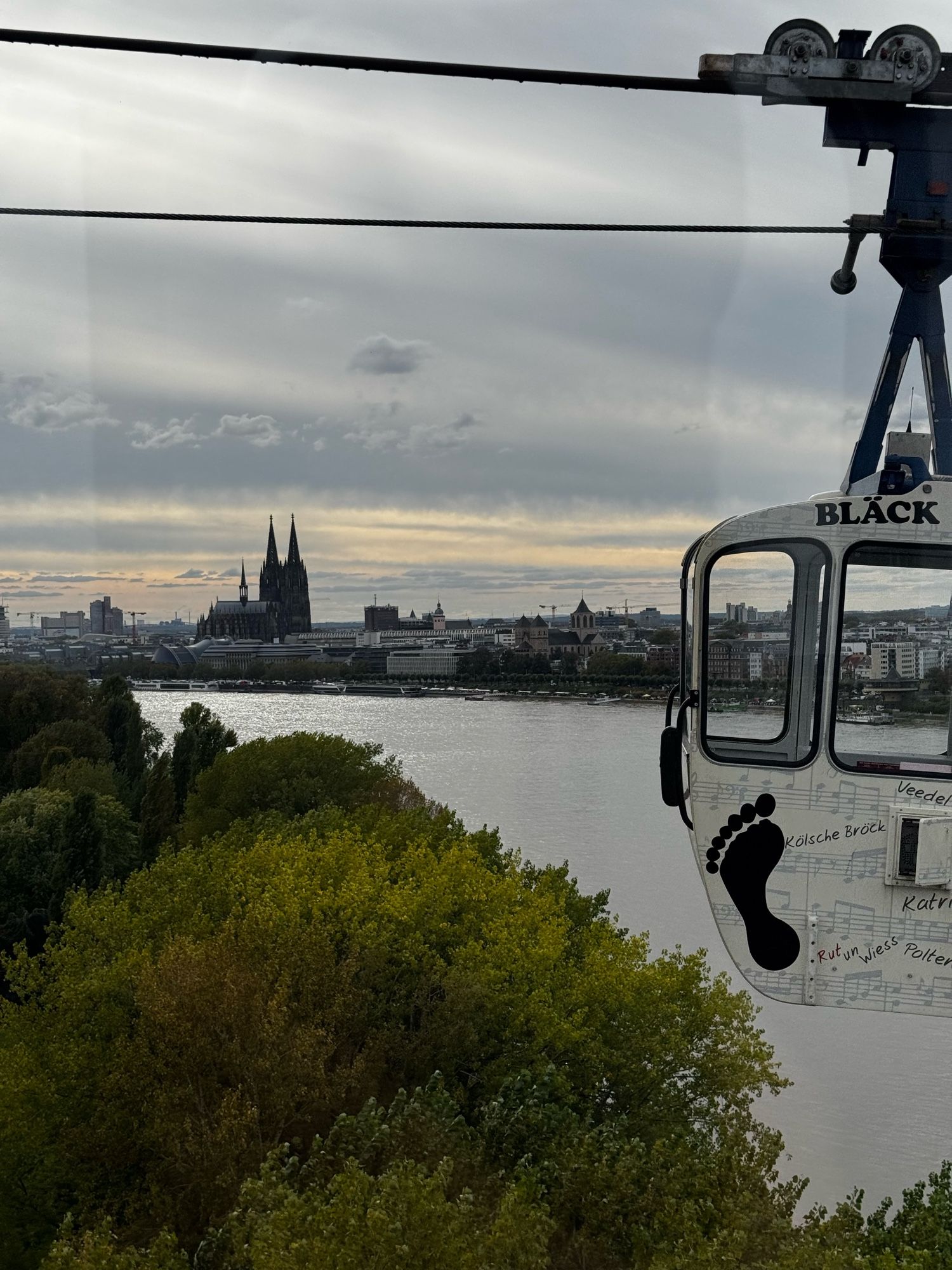 Im Vordergrund eine Gondel, im Hintergrund der Rhein und der Kölner Dom.
Fotografiert aus der Gondel, die bei der Zoobrücke den Rhein überquert.