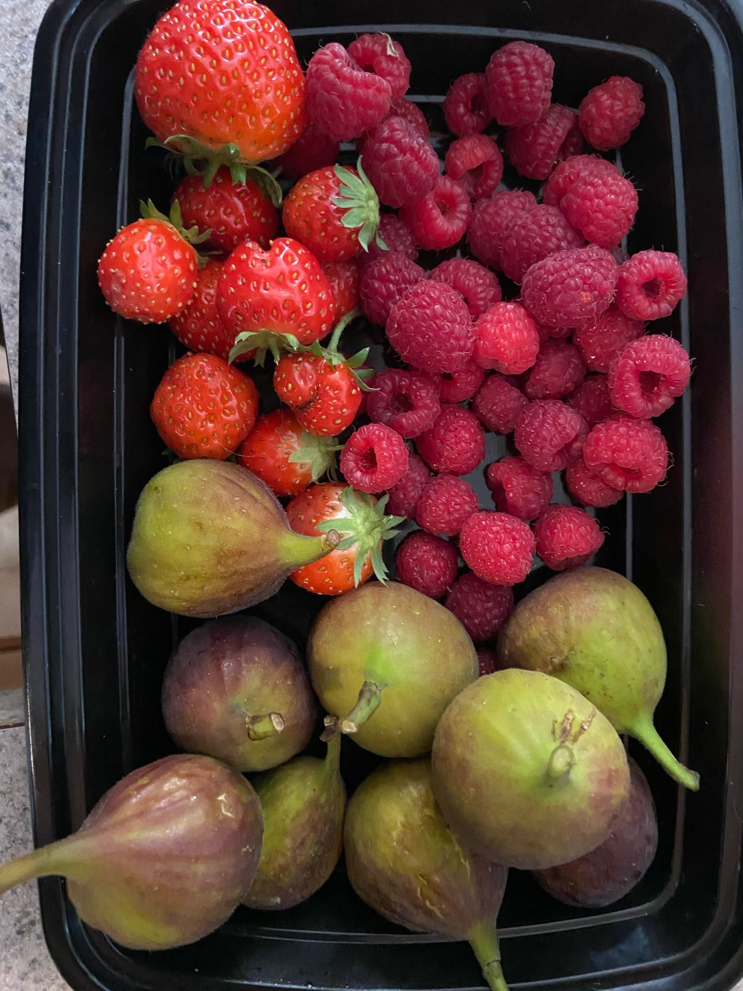 Small black plastic container of strawberries, raspberries, and figs