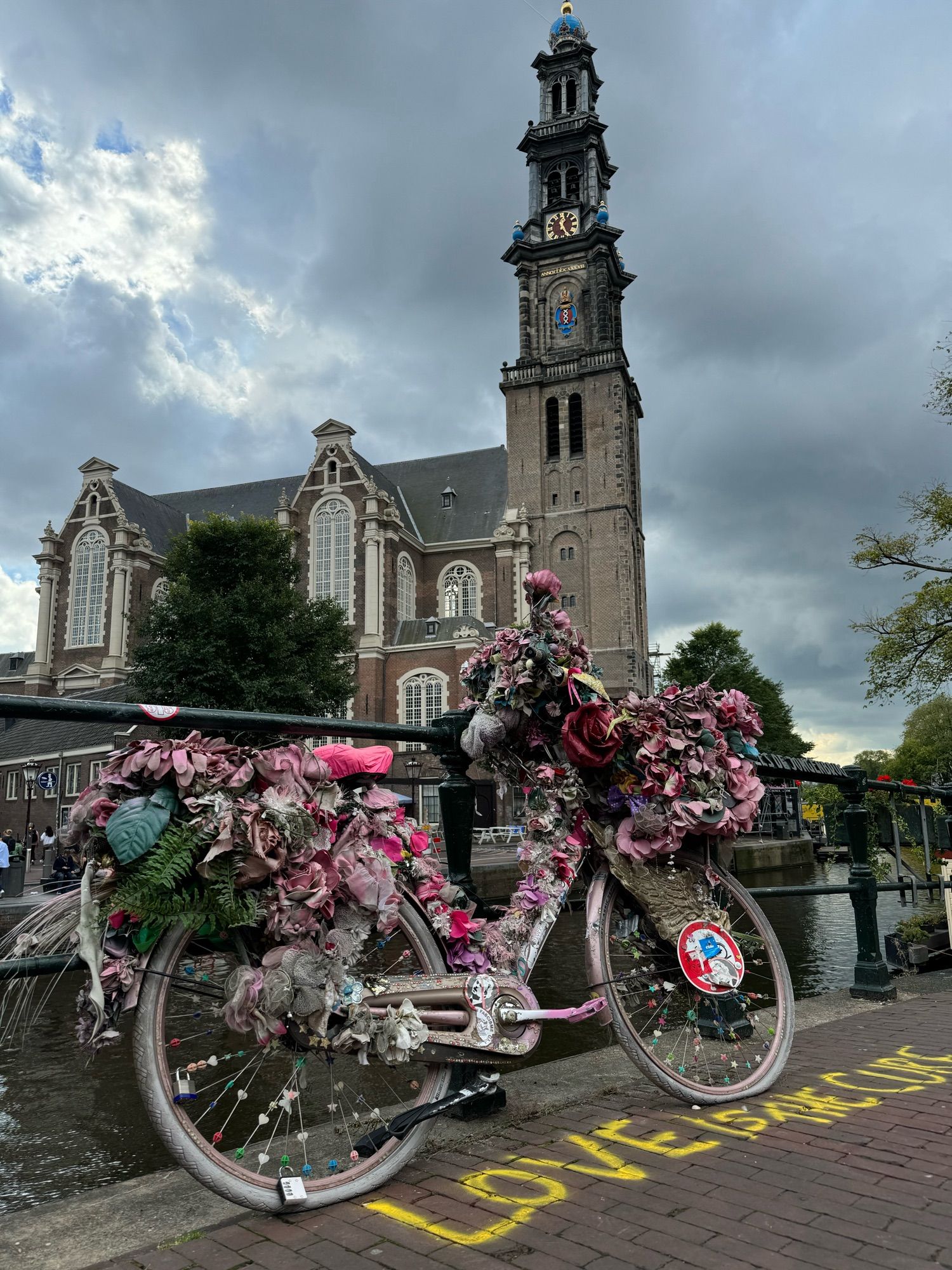 A bicycle with flowers parked in Amsterdam, with “Love is the cure” written on the road in front of it