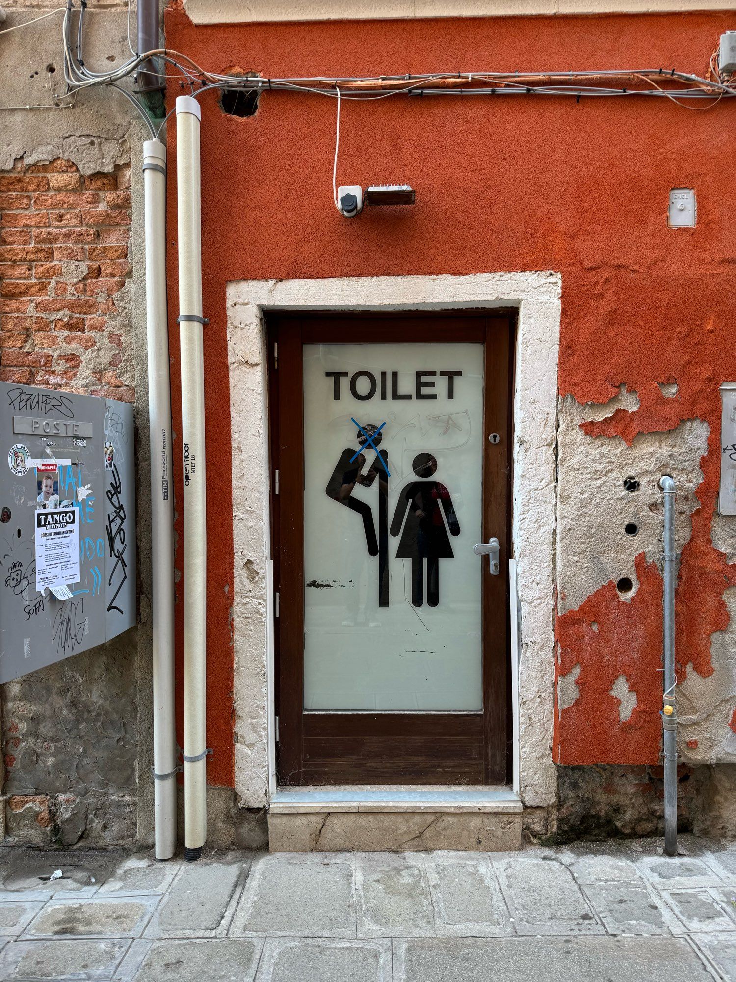 An image on a Venice, Italy bathroom door, showing a male figure peeping over a wall at a female figure