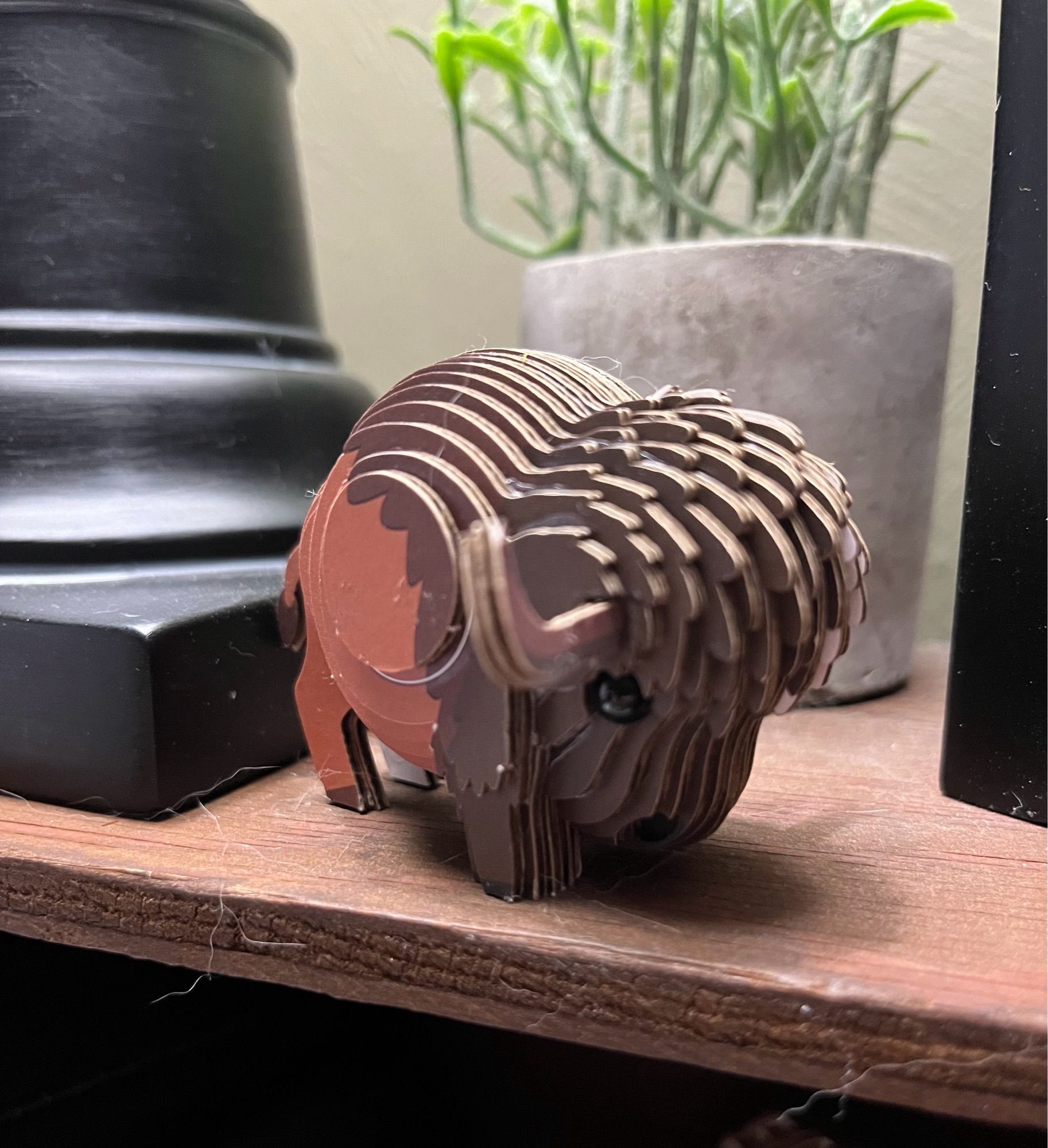 A small, amateurishly assembled wooden bison sculpture rests on a shelf near the base of a lamp