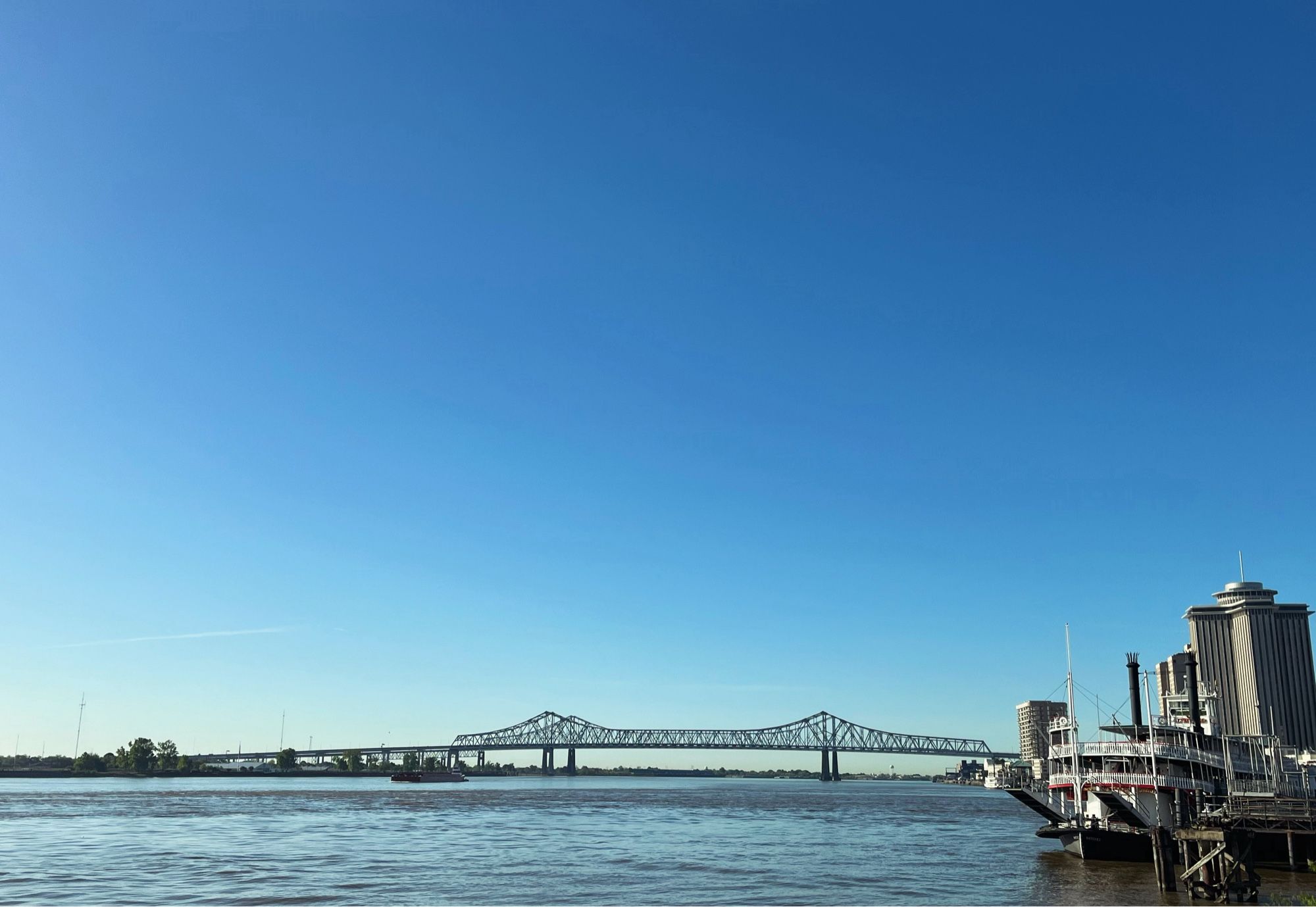 Photo of the Mississippi and the Crescent City Connection bridge, blue skies and calm water.