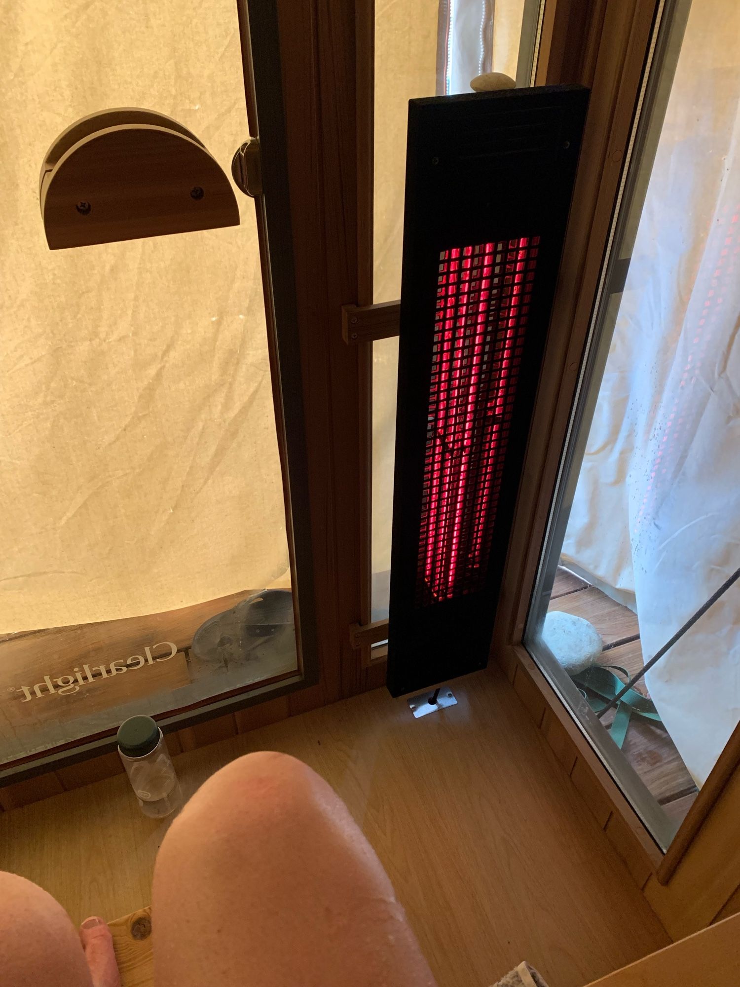 A picture of the inside of a home sauna; you can see the infrared heaters, glass walls (although, covered) and my knees.