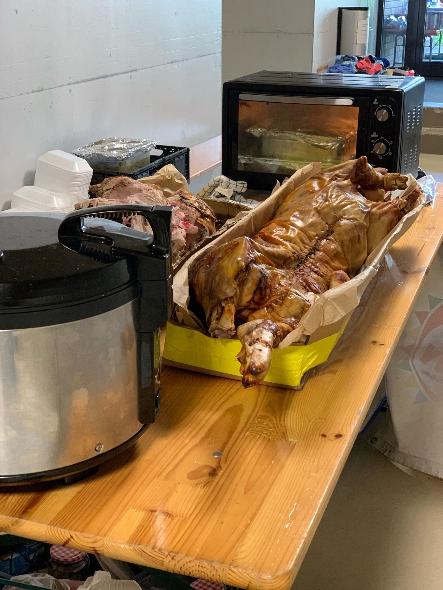 A picture of a whole roasted pig, in the foreground there is a rice cooker, in the background there is an oven.