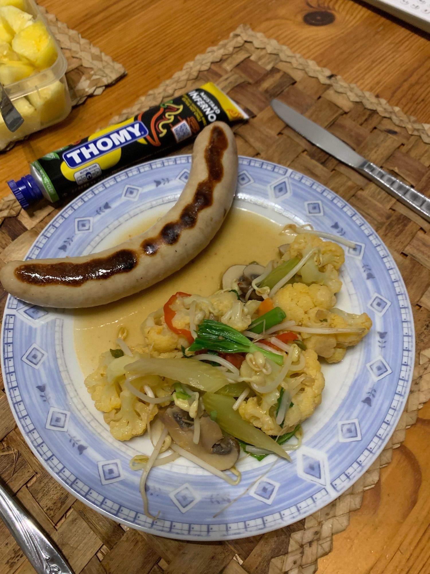 A pic of a plate of vegetables and a bratwurst; in the background is a tube of mustard.